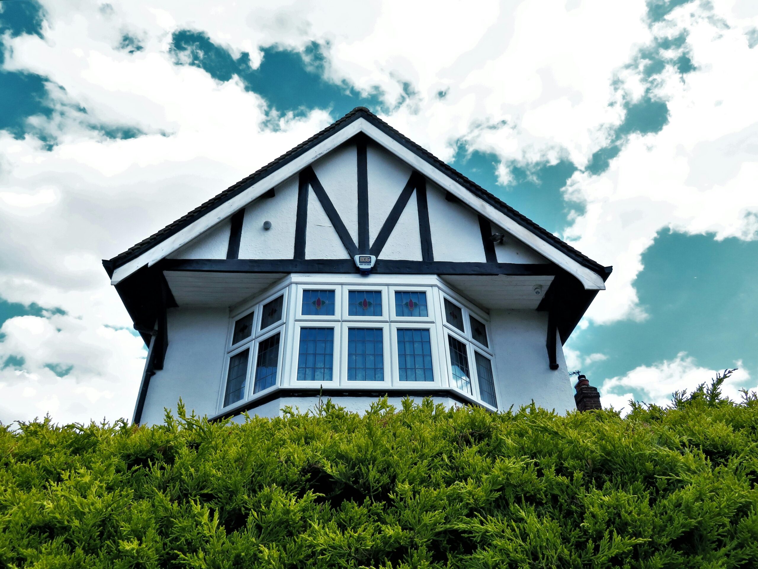 Tudor-style house facade with a bay window against a vibrant sky and greenery.