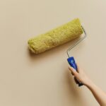A hand using a yellow paint roller to paint a beige wall. Perfect for DIY and home improvement themes.