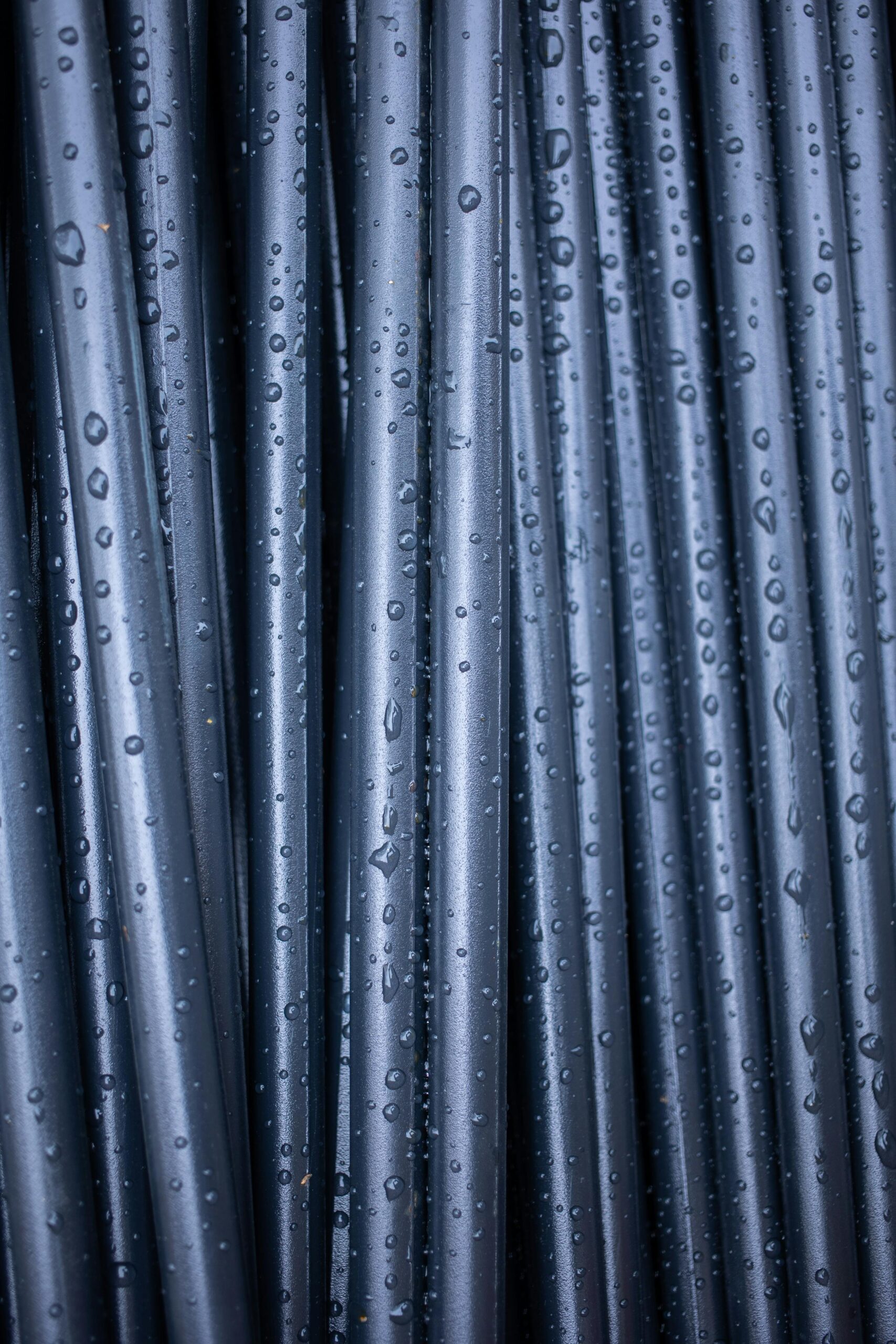 An abstract close-up of vertically arranged wet black pipes with raindrops.